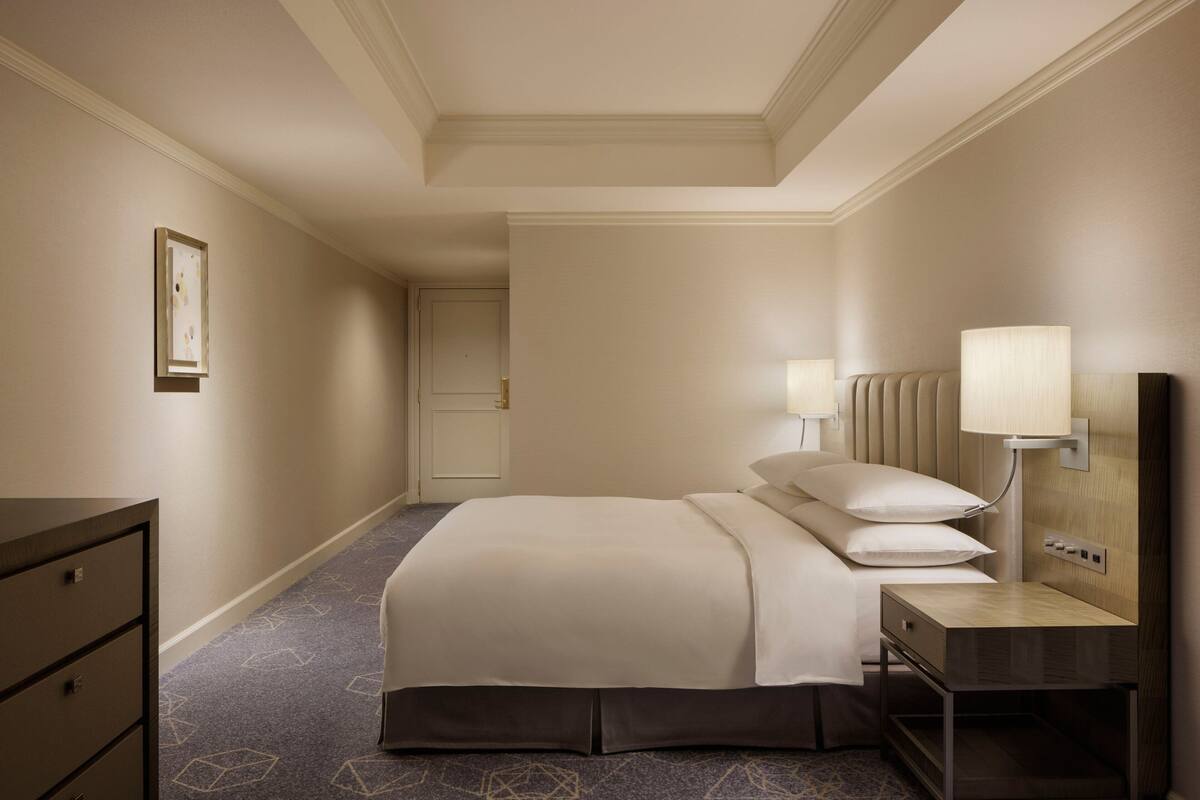 A hotel room with a bed, bedside table, lamp, and a dresser.