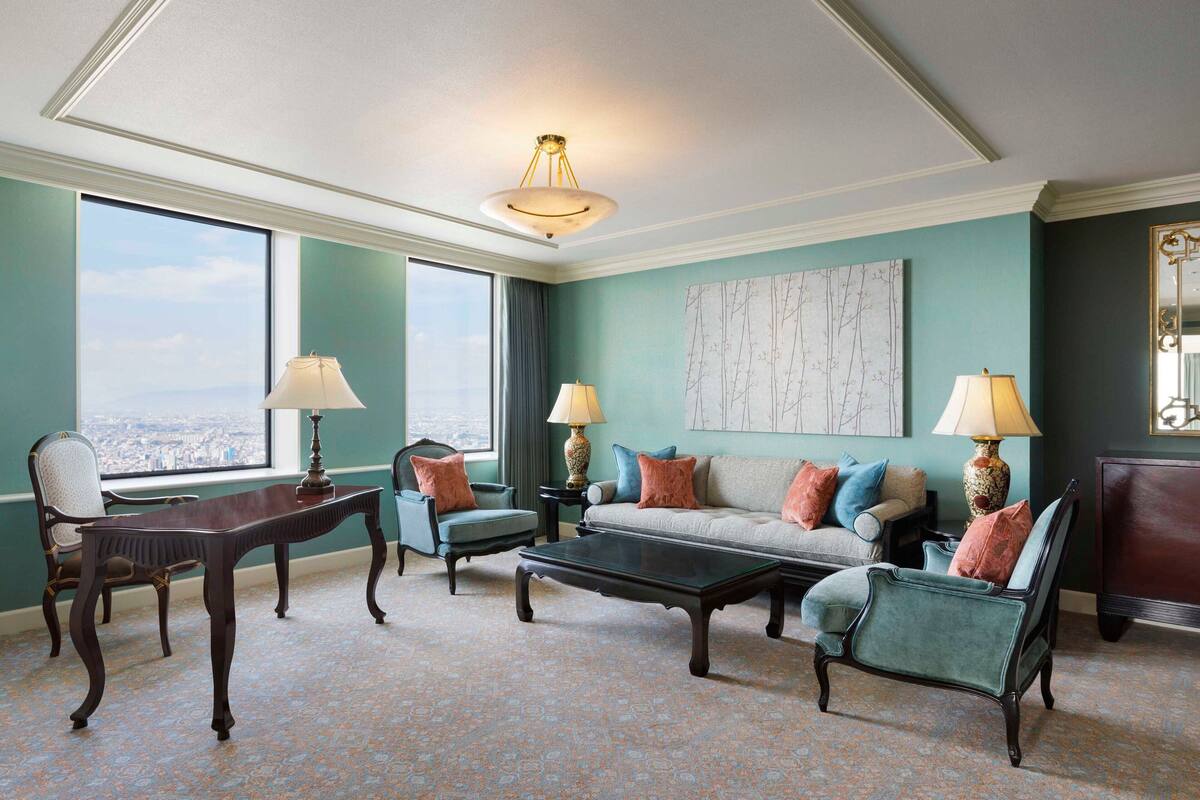 A spacious living room with a large window, a sofa set, a coffee table, and two lamps.