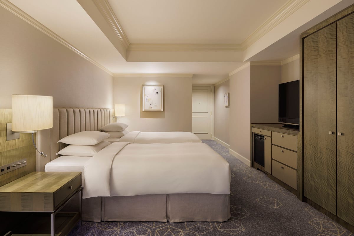 A hotel room with a bed, bedside table, lamp, TV, wardrobe, and a small kitchenette.