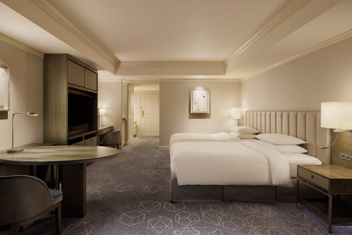 A hotel room with a bed, bedside tables, a desk with a chair, a television, and a patterned carpet.