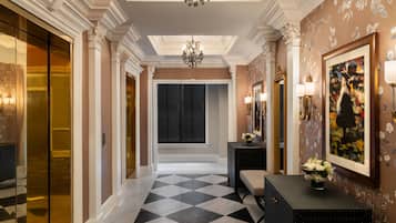 A hallway with a checkered floor, a chandelier, a painting, and a wall with floral wallpaper.