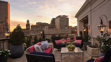 A rooftop terrace with outdoor seating, potted plants, and a city skyline view.