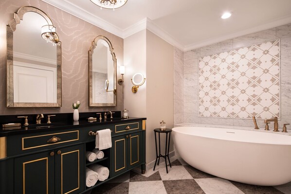 A luxurious bathroom with a freestanding bathtub, double sinks with gold fixtures, and a decorative mirror.