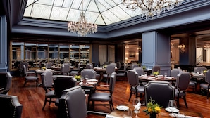 A spacious dining area with multiple tables and chairs, a large chandelier, and a glass ceiling.