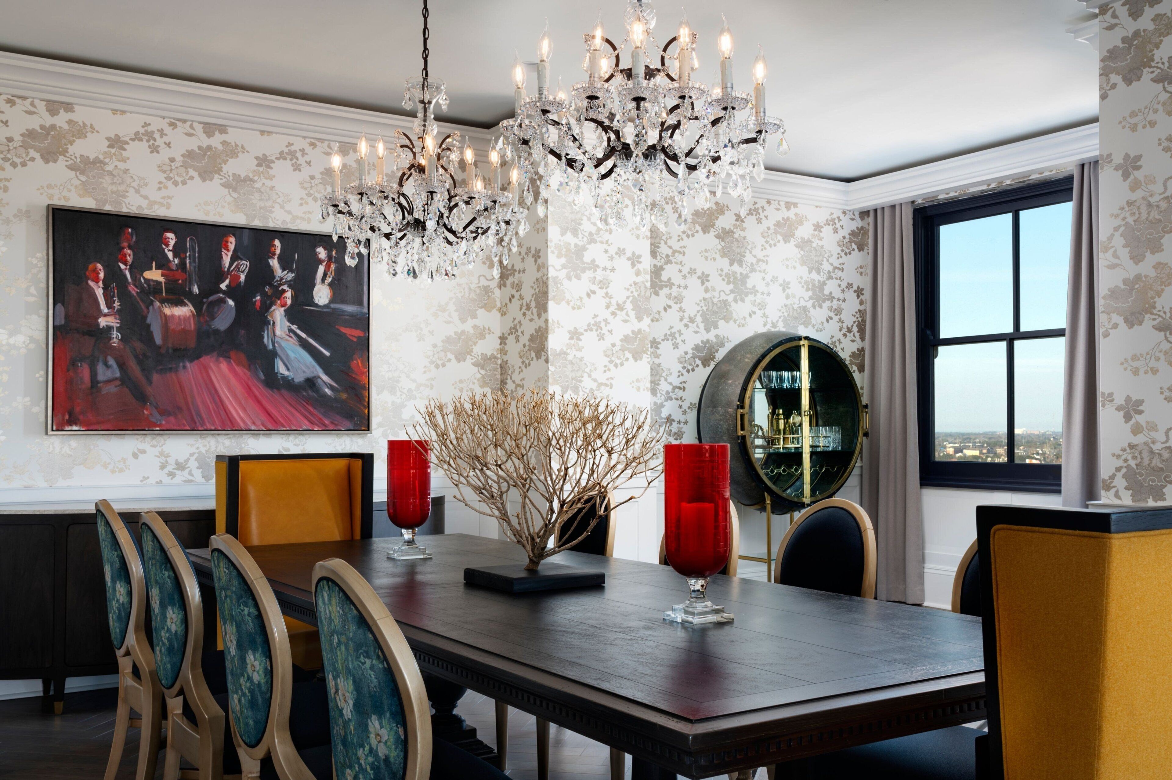 A dining area with a chandelier, floral wallpaper, and a large painting.