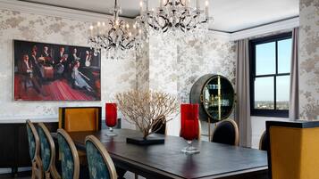 A dining area with a chandelier, floral wallpaper, and a large painting.