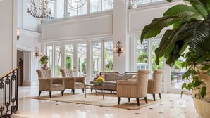 A spacious, elegantly furnished living room with a high ceiling, large windows, and a polished floor.