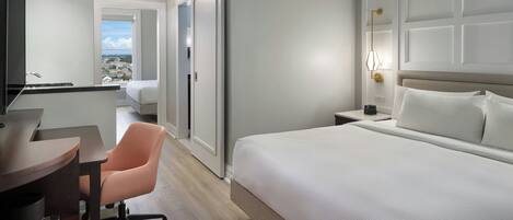 Habitación de hotel con cama, escritorio con silla, mesita de noche y vista de la ciudad a través de una puerta.