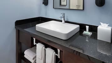 A bathroom with a white sink, dark countertop, and a towel rack with folded towels.