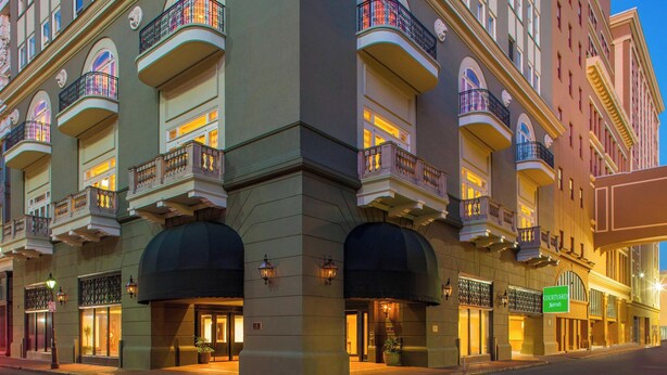 Un hotel de varios pisos con balcones, ventanas amplias y un cartel que indica un patio.