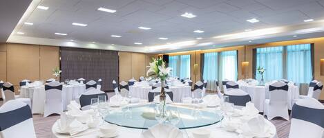 A banquet hall with round tables, white tablecloths, and chairs with dark sashes.
