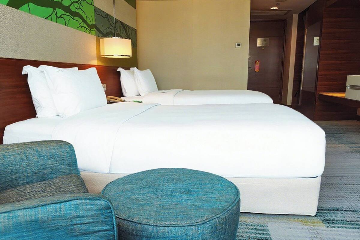 A hotel room with two beds, a blue armchair, and a small ottoman.