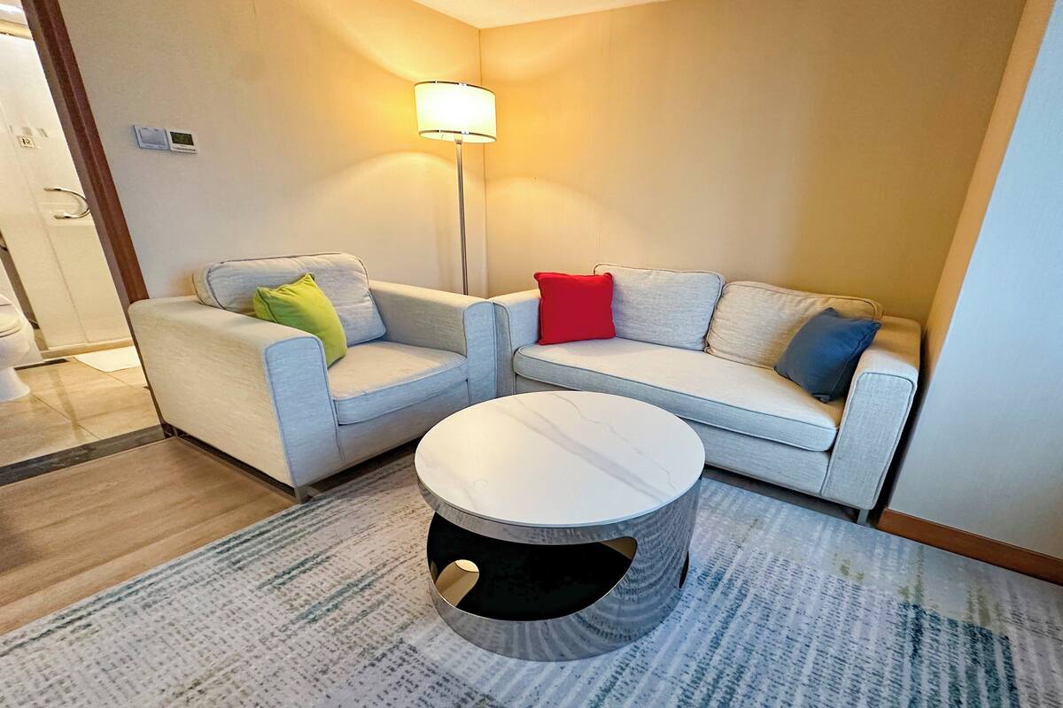 A hotel room with two sofas, a round coffee table, and a floor lamp.