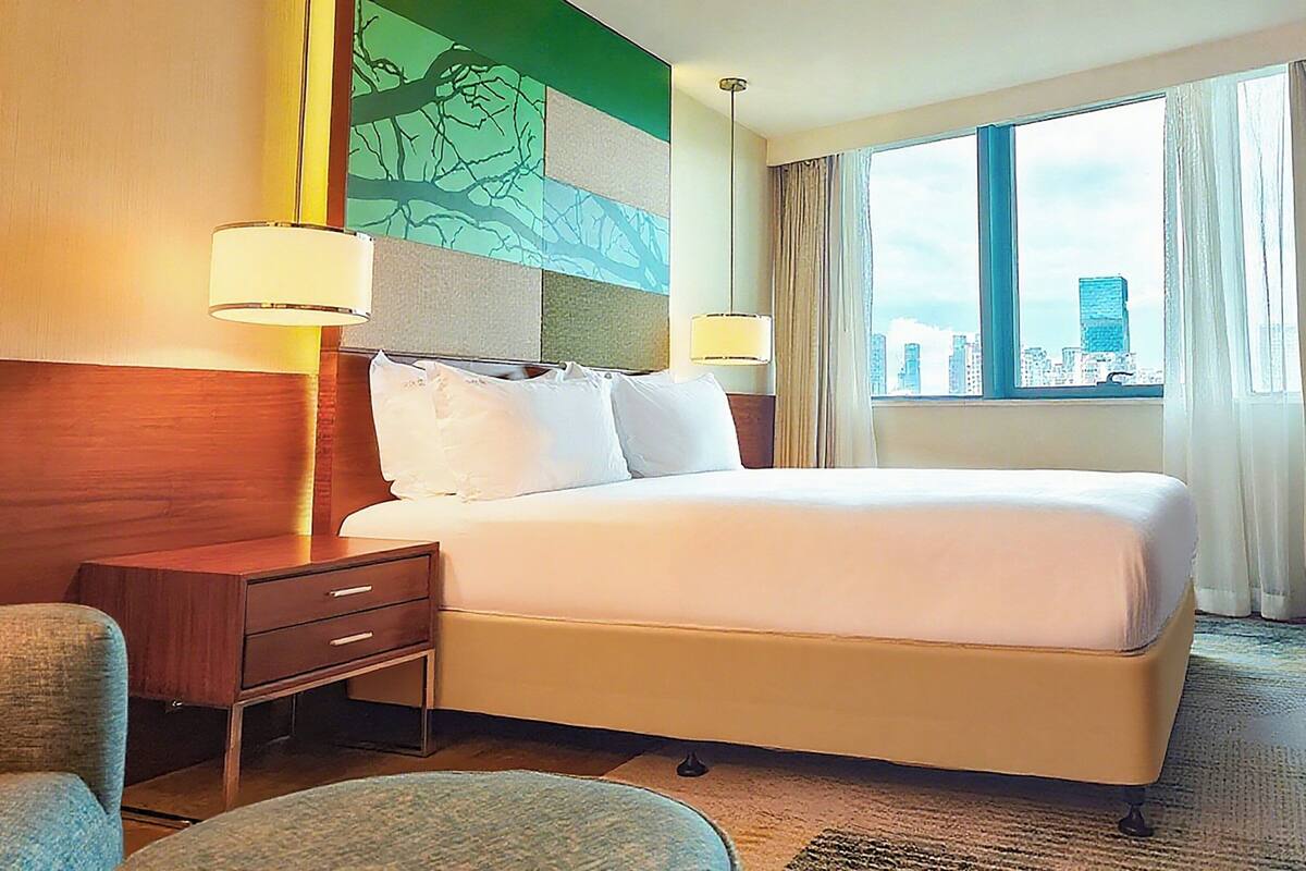 A hotel room with a large bed, two bedside tables with lamps, a chair, and a view of the city through a window.