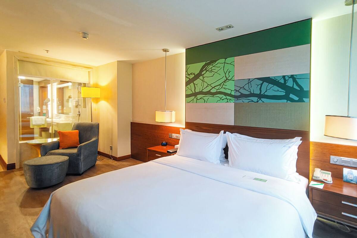 A hotel room with a large bed, a chair, a desk, and a mirror.