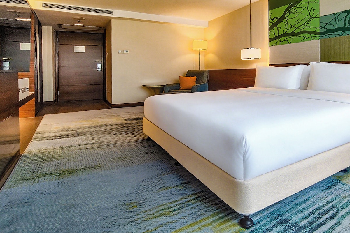 A hotel room with a large bed, a nightstand, a lamp, and a door.