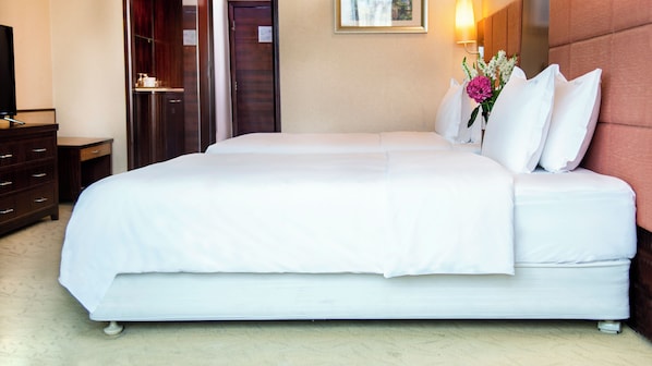 A double bed with white bedding, a nightstand with a lamp, and a dresser with drawers.