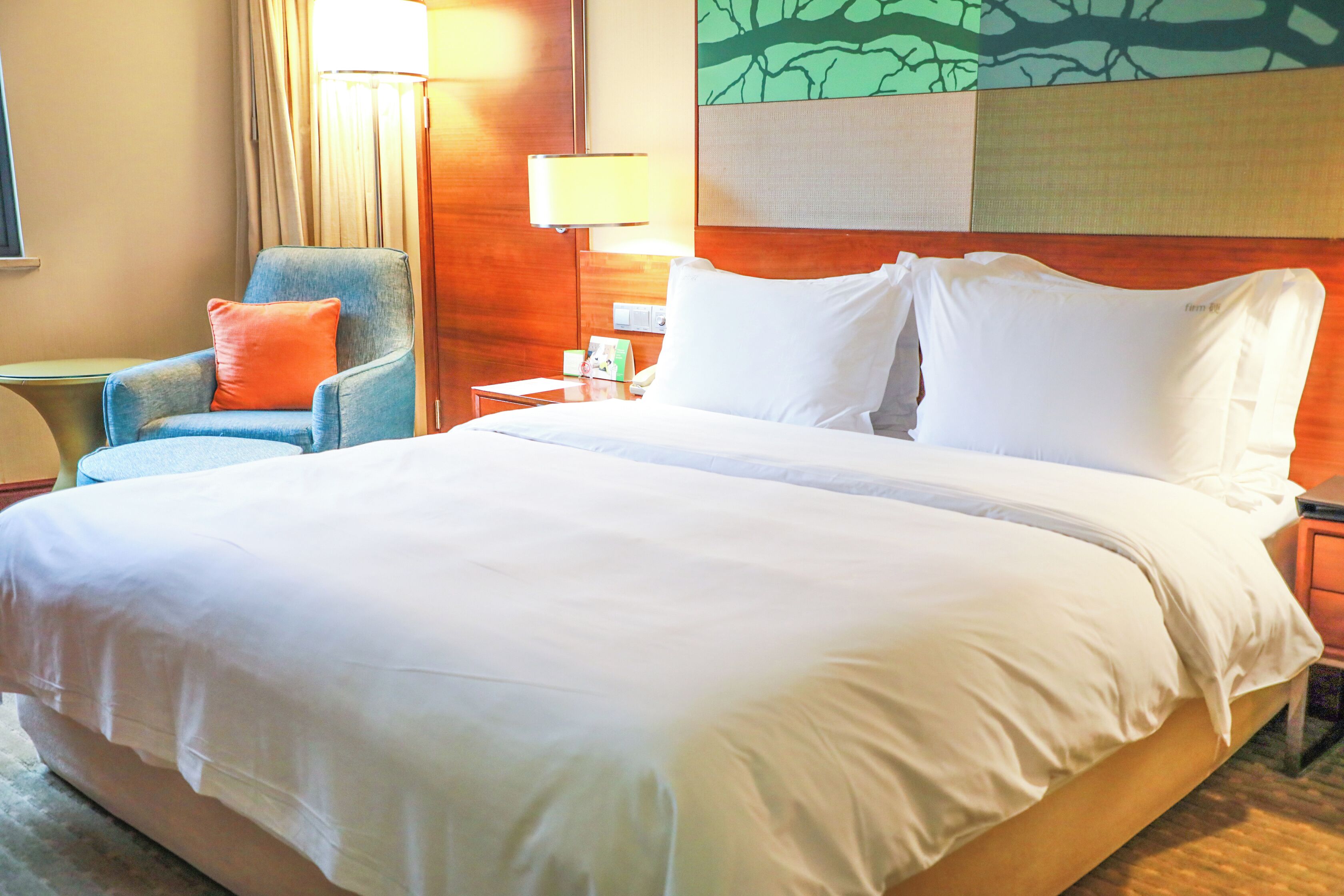 A hotel room with a large bed, a chair, a nightstand, and a lamp.