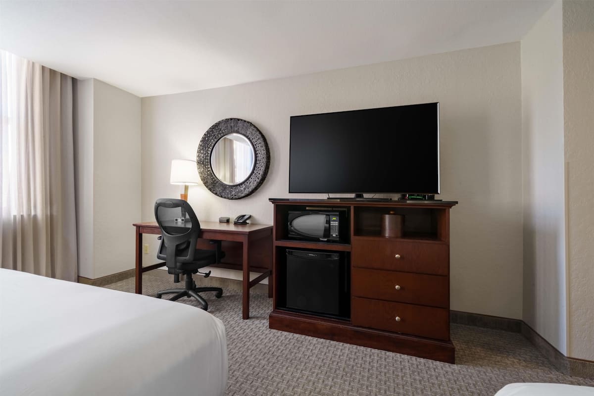A hotel room with a bed, a desk with a chair, a television, a microwave, and a small refrigerator.