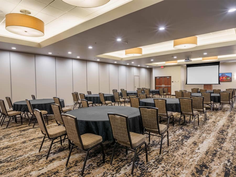 A conference room with round tables and chairs, a projector screen, and a carpeted floor.
