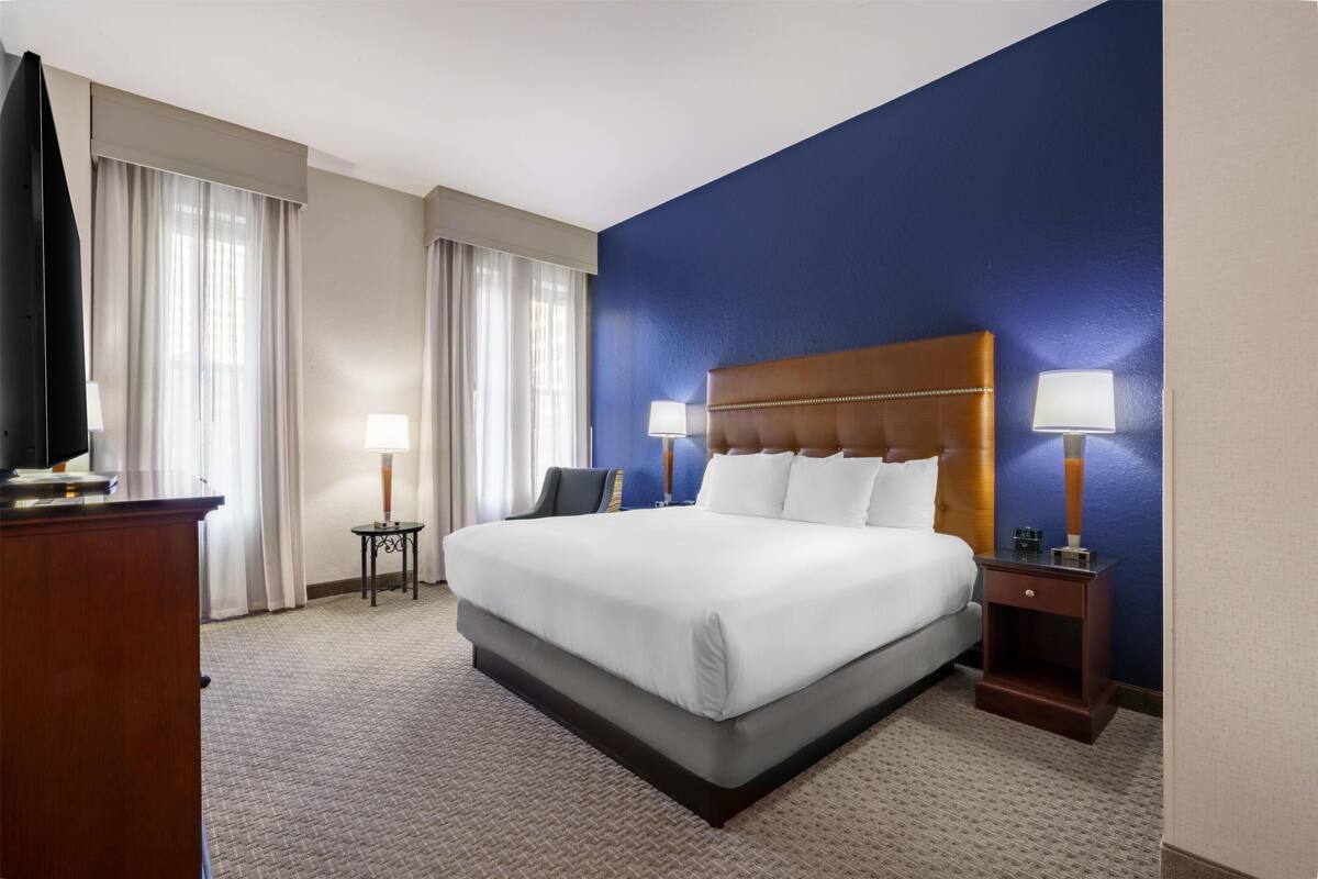 A hotel room with a large bed, two bedside tables with lamps, a flat-screen TV, and a wooden dresser.