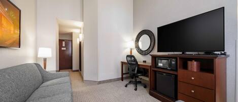 Hotelkamer met een grijze bank, een kleinere grijze fauteuil, een bureau met stoel, een flatscreen televisie, een magnetron en een houten kast.