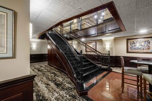 A grand staircase with a polished floor, a dining area with a round table, and a large framed painting on the wall. - Drury Plaza Hotel New Orleans (New Orleans)