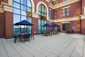 A courtyard with brick walls, large windows, and outdoor seating with umbrellas.