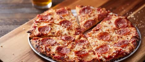 A pepperoni pizza on a metal plate on a wooden table.