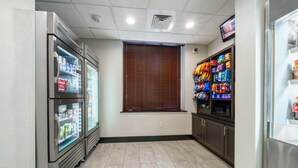 Una habitación limpia y bien iluminada, con refrigerador, máquinas expendedoras y microondas.