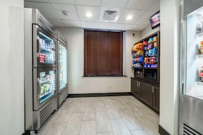 Una habitación limpia y bien iluminada, con refrigerador, máquinas expendedoras y microondas.