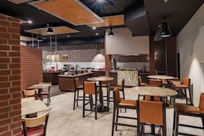 A restaurant with multiple tables and chairs, a kitchen area, and a brick wall. - Drury Plaza Hotel New Orleans (New Orleans)
