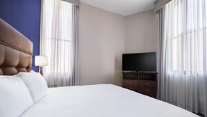 Una habitación de hotel con una cama grande, un televisor de pantalla plana, un aparador de madera y cortinas traslúcidas.