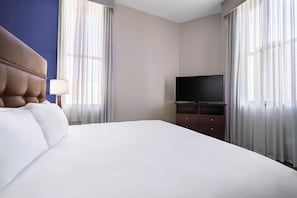 Una habitación de hotel con una cama grande, un televisor de pantalla plana, un aparador de madera y cortinas traslúcidas.