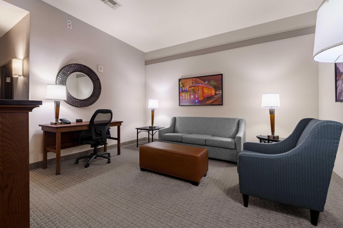 A hotel room with a desk, office chair, sofa, ottoman, and two lamps.