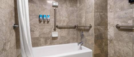 A modern bathroom with a bathtub, a shower, marble walls, and handrails.