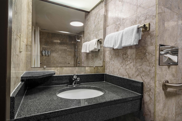 Un baño con lavamanos de encimera de granito, un espejo y dos toallas colgadas en ganchos.