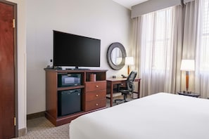 A hotel room with a bed, a flat-screen TV, a microwave, a refrigerator, a desk with a chair, and a large mirror. - Drury Plaza Hotel New Orleans (New Orleans)