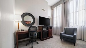 Habitación de hotel con escritorio, silla, televisión y un amplio ventanal con cortinas.