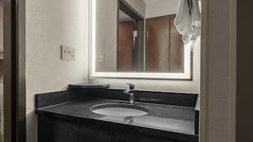 A bathroom with a granite countertop, a sink, a mirror, and a towel hanging on a rack.