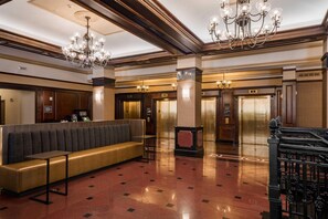 Eine Lobby mit einer Bank, Kronleuchtern, Aufzügen und einem Empfangstresen.