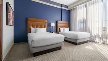 A hotel room with two beds, a large window with sheer curtains, a framed picture on the wall, and a carpeted floor.
