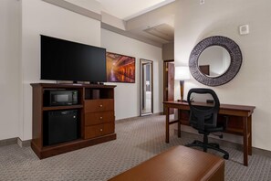 A hotel room with a flat-screen TV, a microwave, a small refrigerator, a wooden desk, a black office chair, a round mirror, and a large painting on the wall. - Drury Plaza Hotel New Orleans (New Orleans)