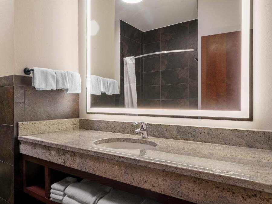 A bathroom with a granite countertop sink, a mirror, and a shower area.