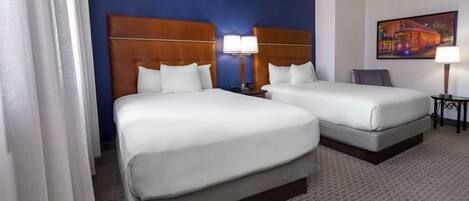 Habitación de hotel con dos camas, una mesita de noche con lámparas, un cuadro en la pared y piso alfombrado.