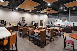A restaurant with multiple dining tables and chairs, a bar area, and a kitchen in the background.