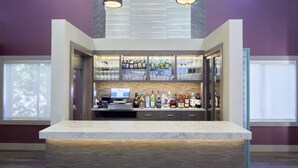 Un espace bar doté d’un comptoir en marbre, d’étagères remplies de bouteilles d’alcool et d’une caisse enregistreuse.