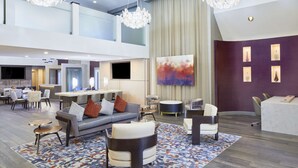 Un hall d’entrée spacieux avec un plafond haut, des meubles modernes, une grande peinture abstraite et un téléviseur à écran plat fixé au mur.