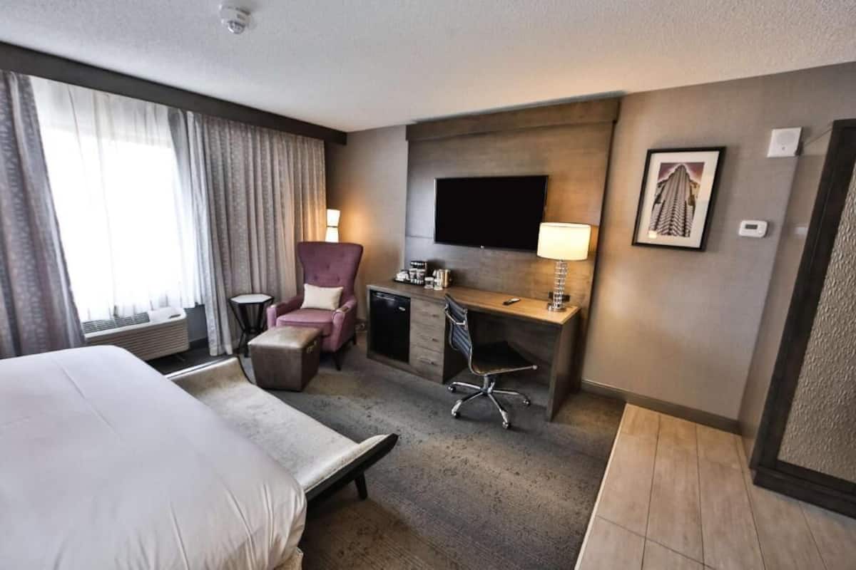 A hotel room with a bed, a desk, a chair, a TV, and a window with curtains.