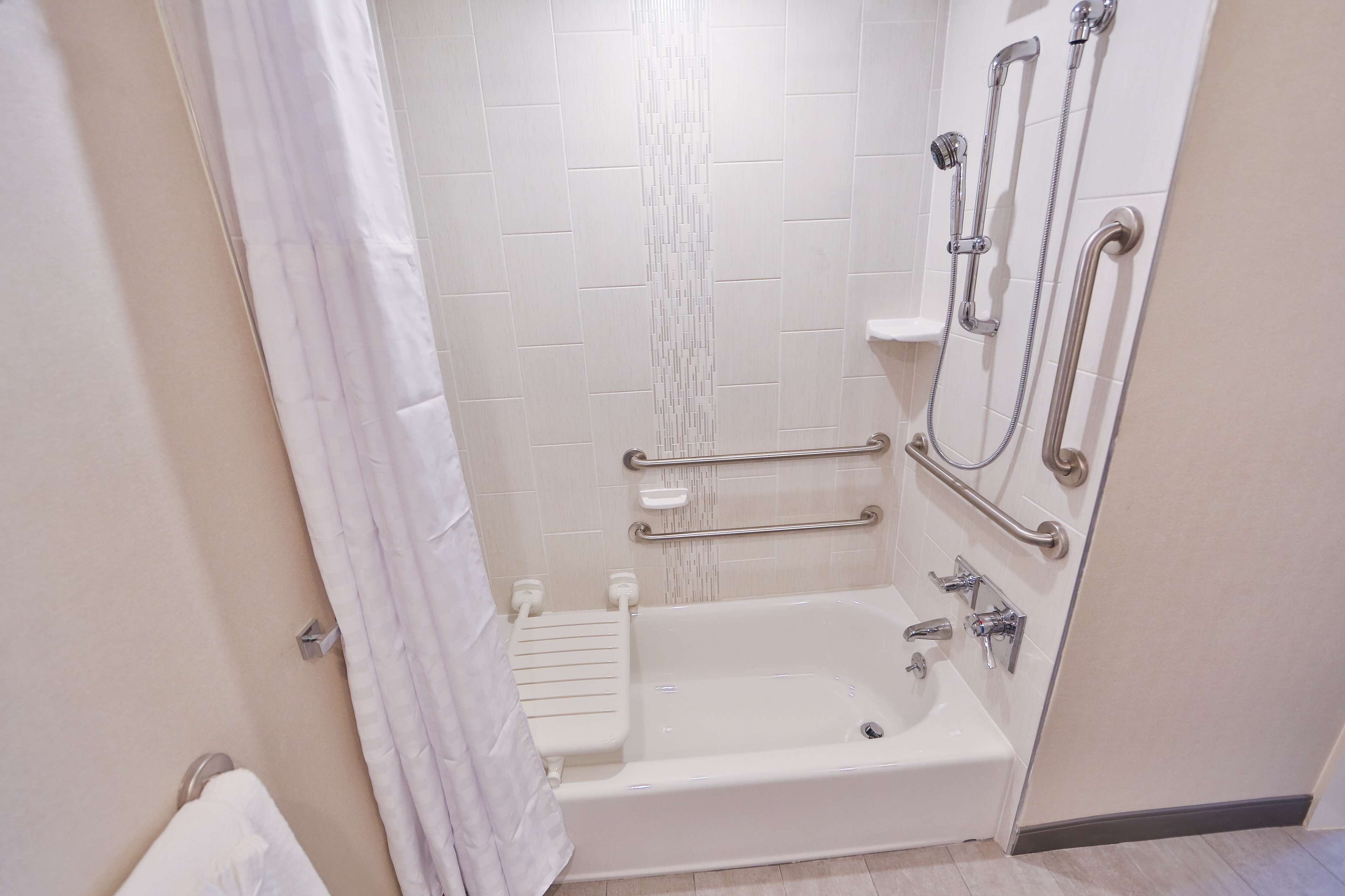 Une salle de bain avec une baignoire blanche, des barres d’appui, une pomme de douche et un porte-serviettes.